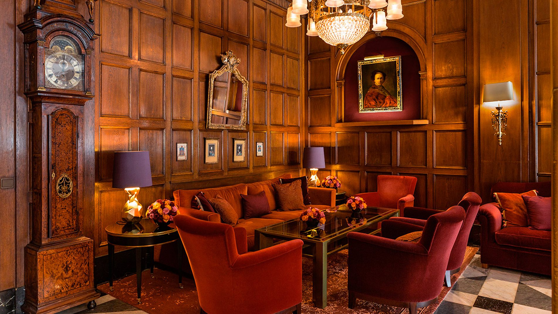 Holzvertäfelter Raum mit roten Sesseln und Sofas in der Wohnhalle im Hotel Vier Jahreszeiten