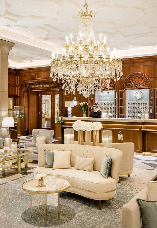 Elegant lobby area at Hotel Vier Jahreszeiten Hamburg with a chandelier, seating areas and reception in the background.