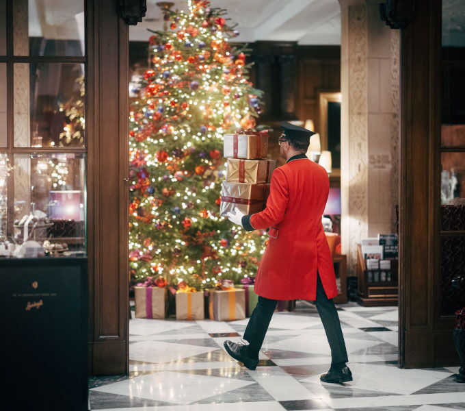 Doorman at Hotel Vier Jahreszeiten Hamburg carrying festive gifts in front of the Christmas tree.