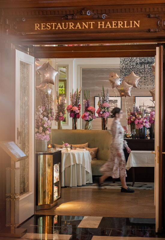 Blick in den Eingangsbereich des Restaurant Haerlin im Hotel Vier Jahreszeiten Hamburg mit gedeckten Tischen, Blumendekoration und Servicepersonal.