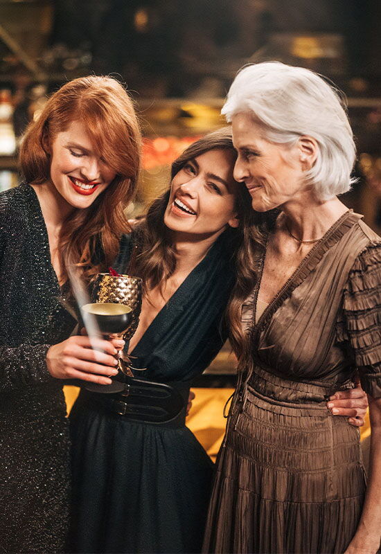 Three guests in elegant evening attire stand together laughing and enjoying drinks at Hotel Vier Jahreszeiten Hamburg.