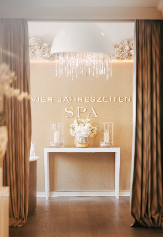 Entrance area of the Vier Jahreszeiten Spa with decorative lighting, floral arrangement and wall lettering.