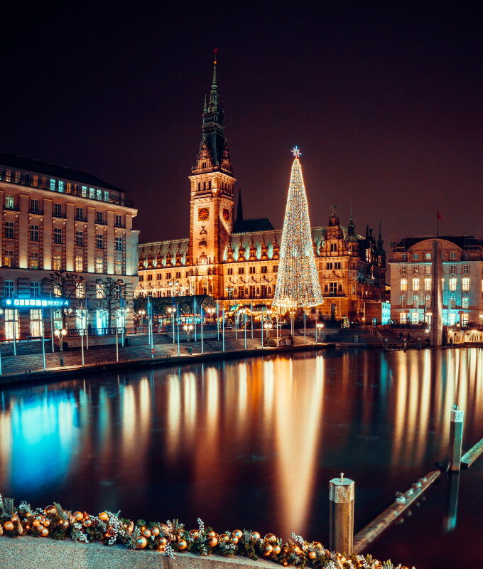 Beleuchtetes Hamburger Rathaus mit festlichem Weihnachtsbaum am Wasser bei Nacht