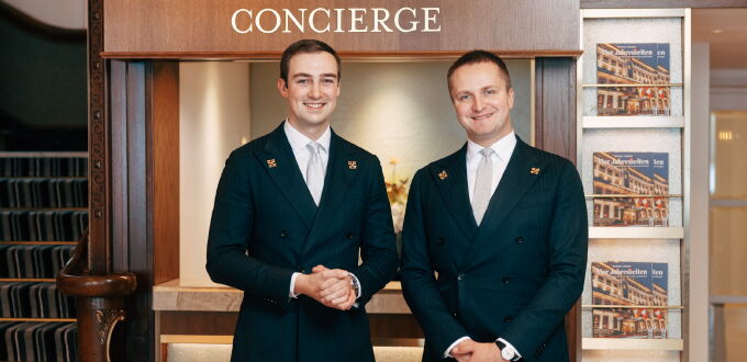 Zwei Concierges des Hotel Vier Jahreszeiten Hamburg stehen lächelnd am Concierge-Schalter