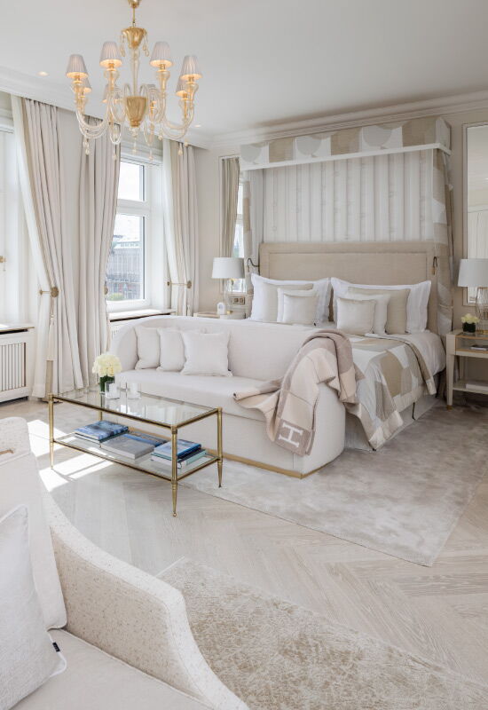 Helle Suite im Hotel Vier Jahreszeiten Hamburg mit Doppelbett, Sitzbereich, Kronleuchter und eleganter Einrichtung.