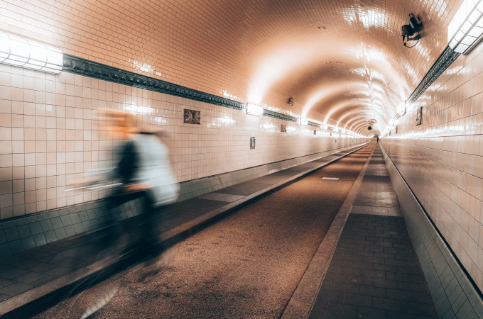 Ein Radfahrer saust in einem langen, gekachelten unterirdischen Tunnel mit heller, gleichmäßiger Beleuchtung vorbei.