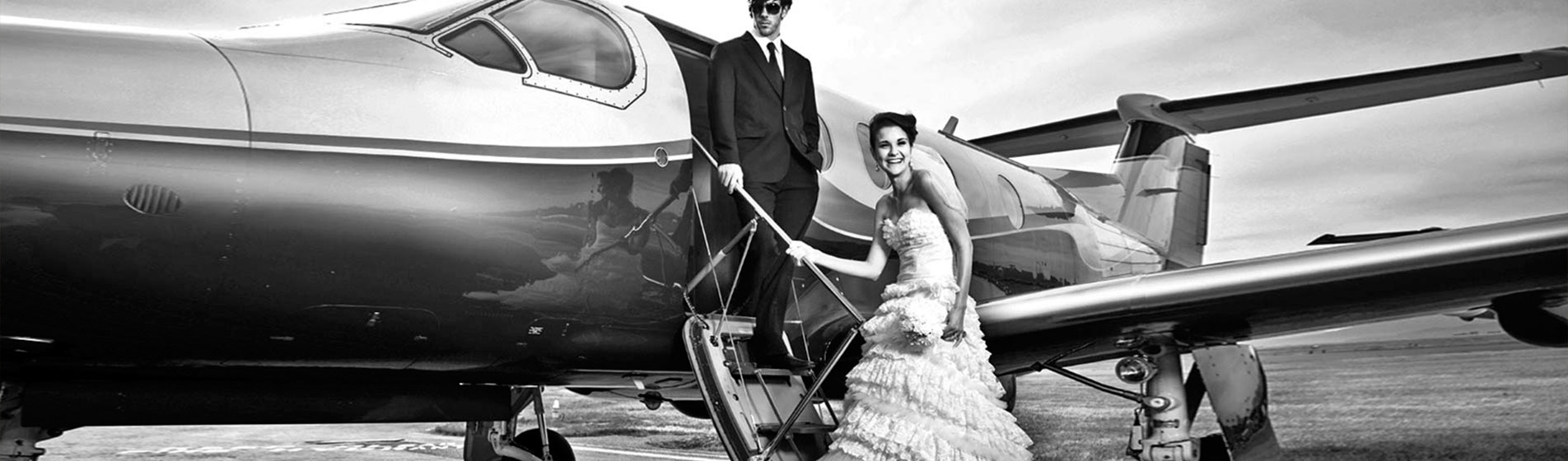 Schwarzweiß Aufnahme eines Brautpaares auf den Treppen eines Privatflugzeugs