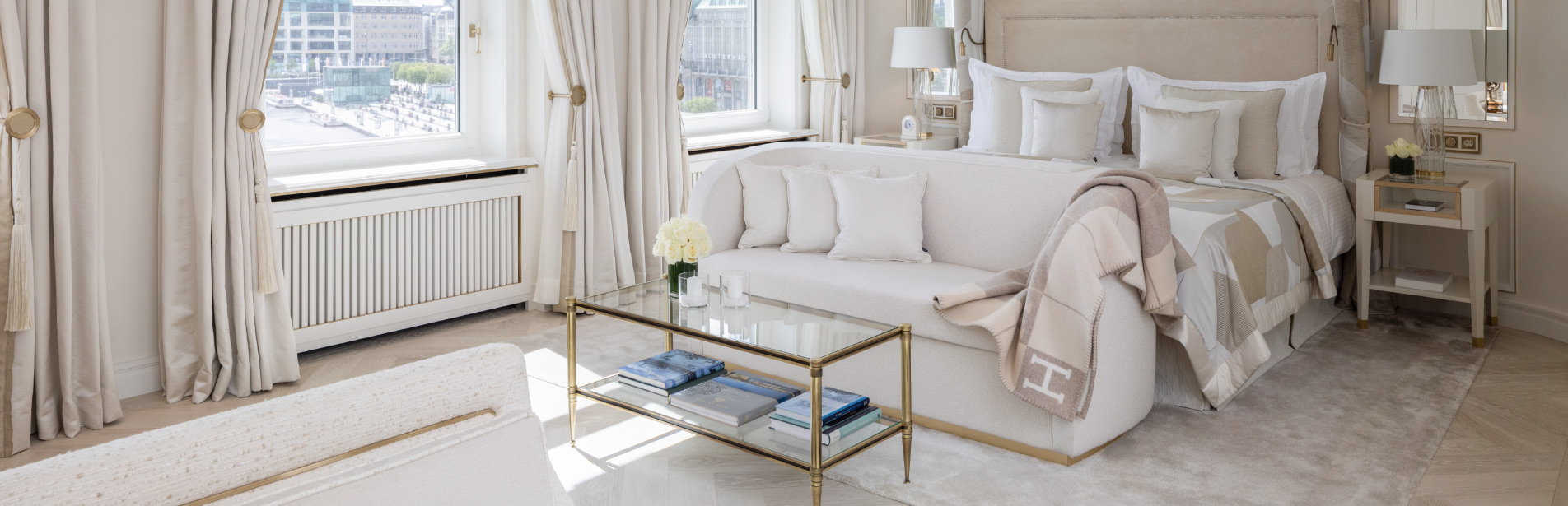 Bright suite at Hotel Vier Jahreszeiten Hamburg with a double bed, seating area, chandelier and elegant interior.